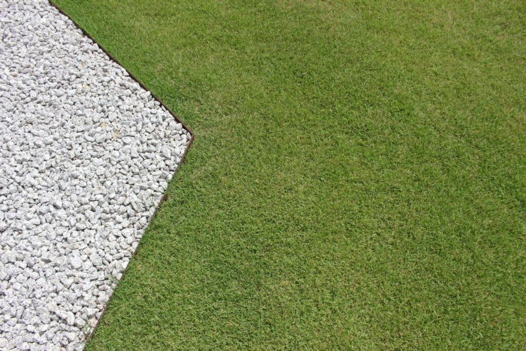 5 Small Garden Ideas on a Budget 2 | The Rock Garden closeup of a crisp, angular border dividing a green lawn from a bed of white landscape rocks.