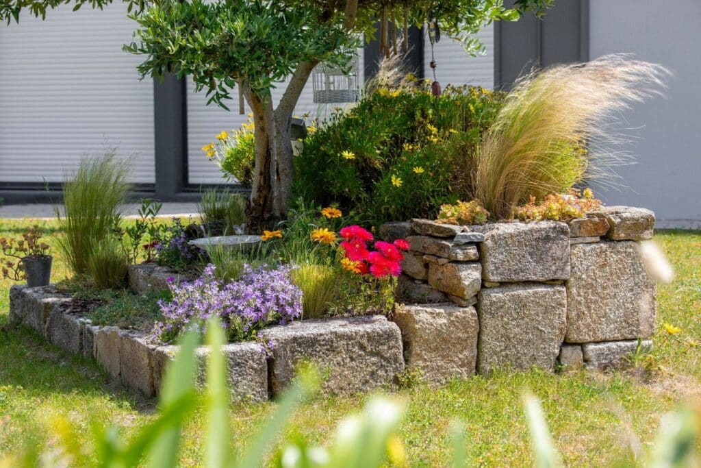 5 Small Garden Ideas on a Budget 3 | The Rock Garden hand-built natural stone planters with flowers and grasses in a backyard under a tree