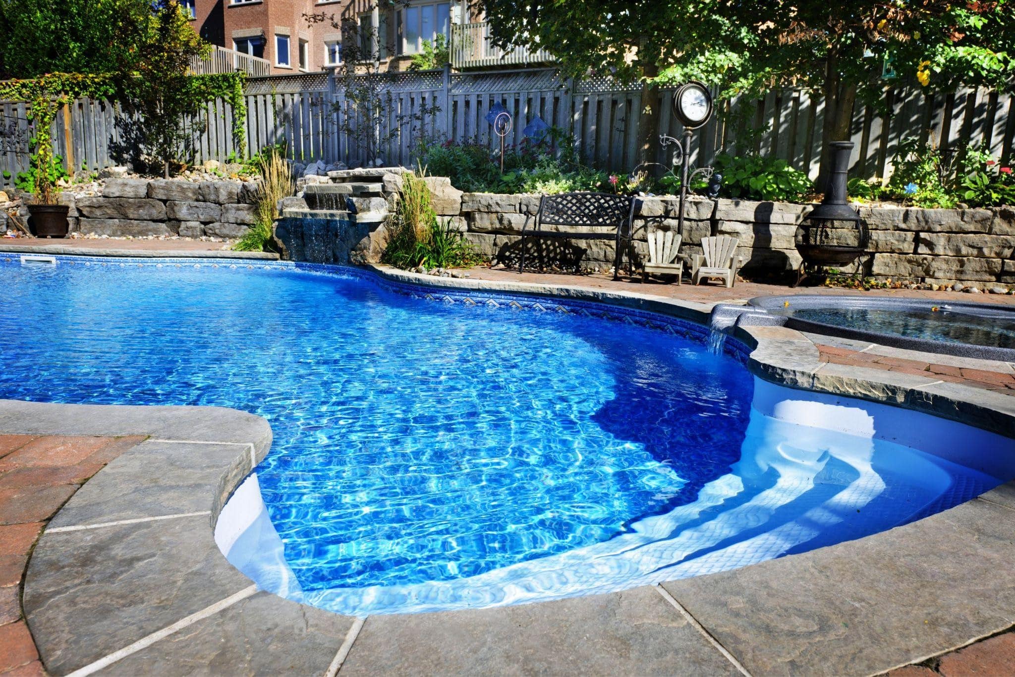 irregular shaped in ground pool with pale brown and tan stone decking